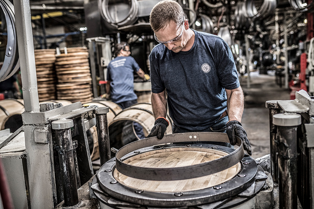Securing top and bottom barrel heads is one of the last touches in barrel production. Here, an employee at Kentucky Cooperage is placing the head hoop on a barrel.