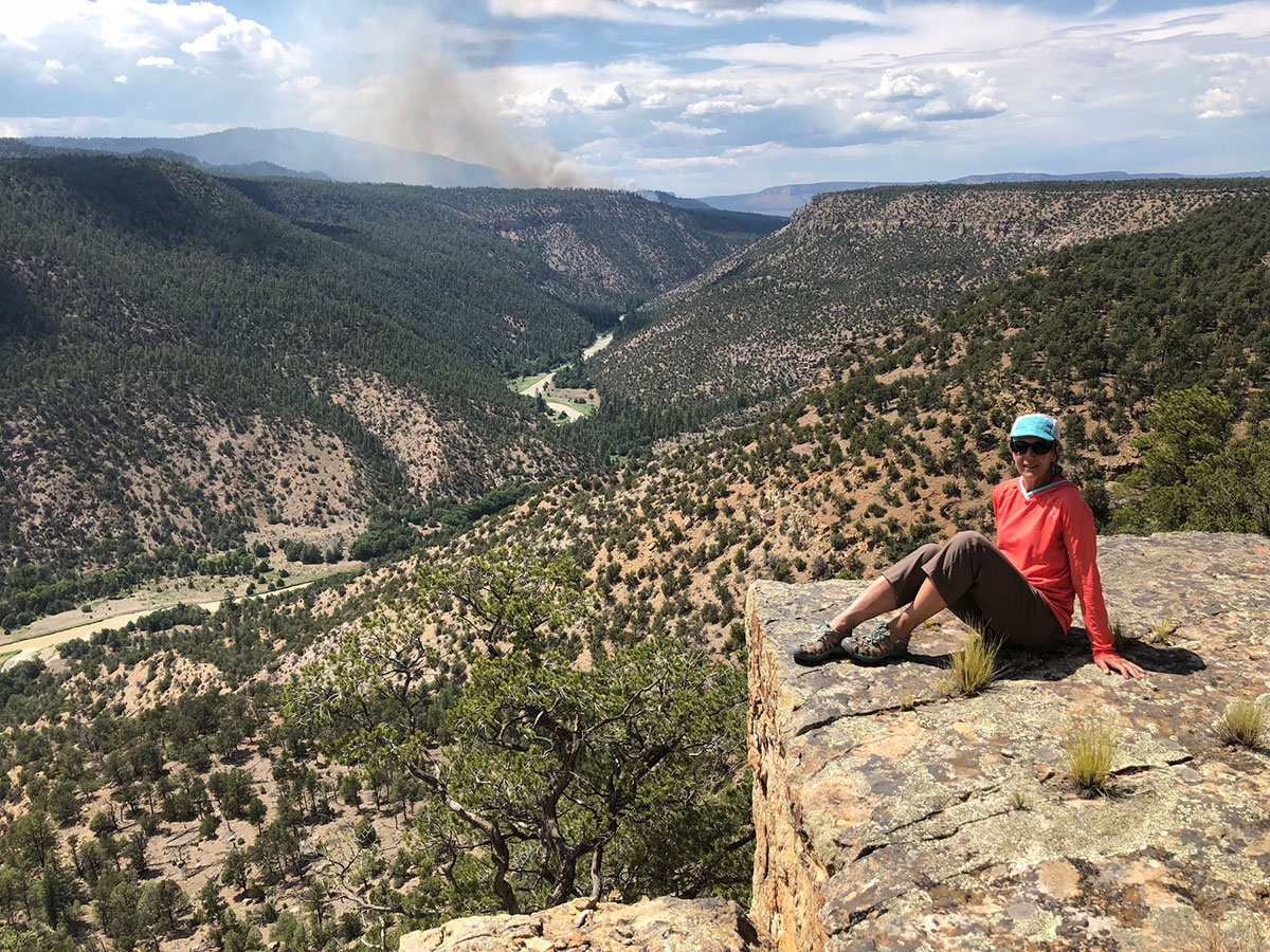 New Mexico State Forester Laura McCarthy at an overlook above the Rio Chama River, a critically important watershed in New Mexico. In the background is smoke from a managed natural wildfire that is helping reduce forest fuels close to the river.
